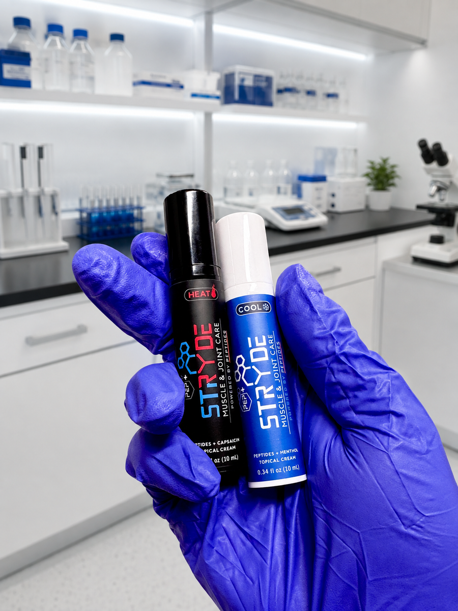 A hand wearing a blue nitrile glove holds two STRYDE essential care products, one HEAT and one COOL, in front of a blurred laboratory background.